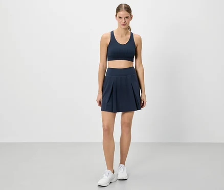 Une femme se tient en tenue de sport devant un fond blanc.