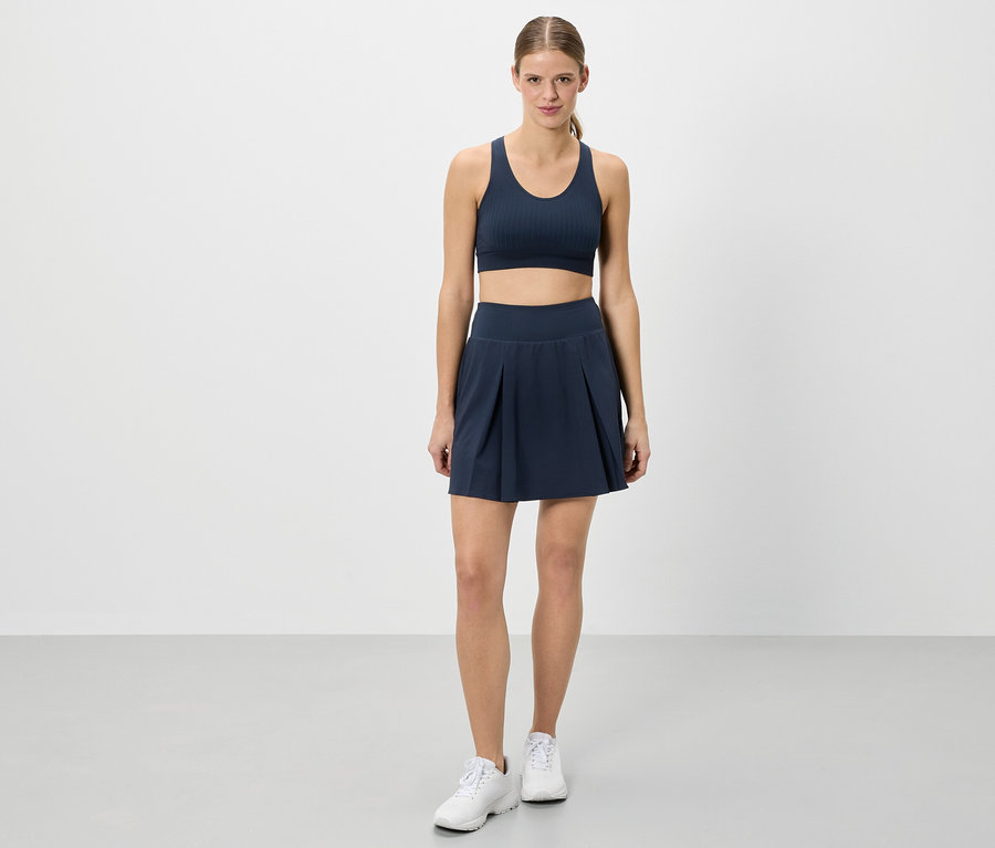 Une femme se tient en tenue de sport devant un fond blanc.