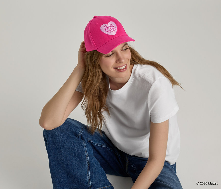 Femme portant une casquette de baseball rose avec un logo en forme de cœur, un t-shirt blanc et un jean.