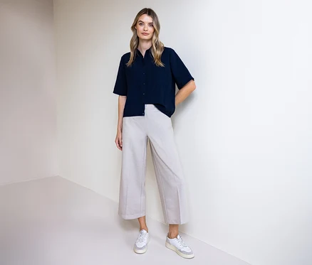 Femme portant un pantalon et un chemisier Street One. Elle se tient devant un mur.