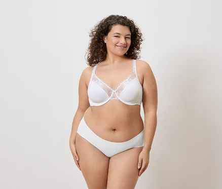 Une femme aux cheveux bouclés porte un soutien-gorge blanc avec des détails en dentelle et des sous-vêtements assortis.