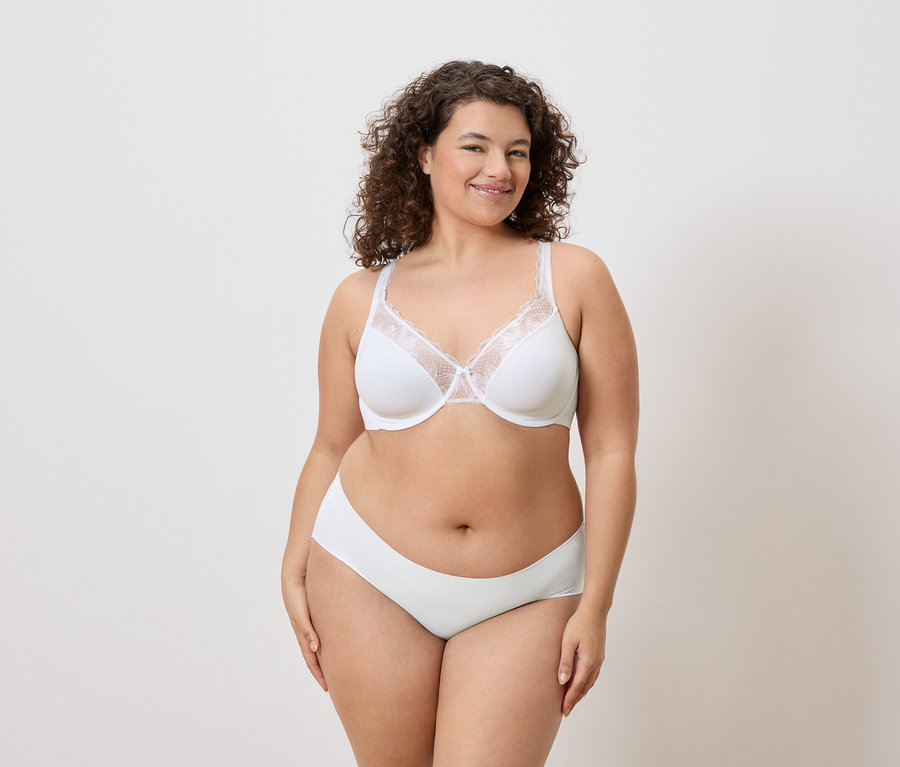 Une femme aux cheveux bouclés porte un soutien-gorge blanc avec des détails en dentelle et des sous-vêtements assortis.