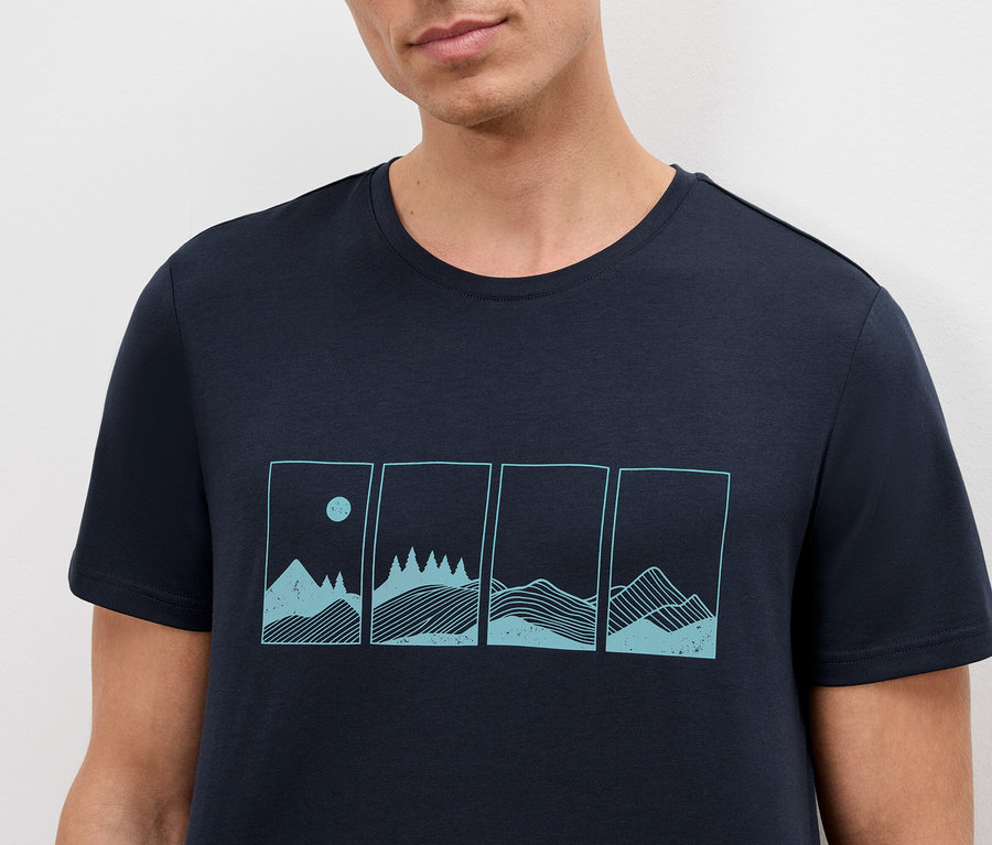Gros plan d'un homme portant un t-shirt bleu marine avec un motif de paysage de montagne.