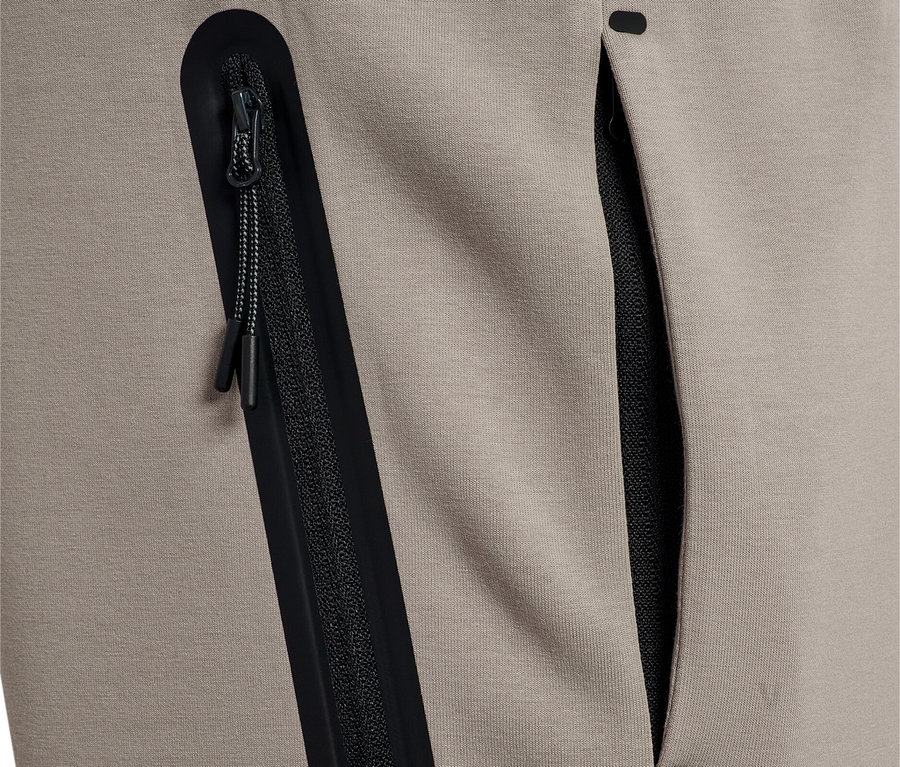 Gros plan d'un pantalon de survêtement beige avec une poche zippée noire et une poche ouverte.