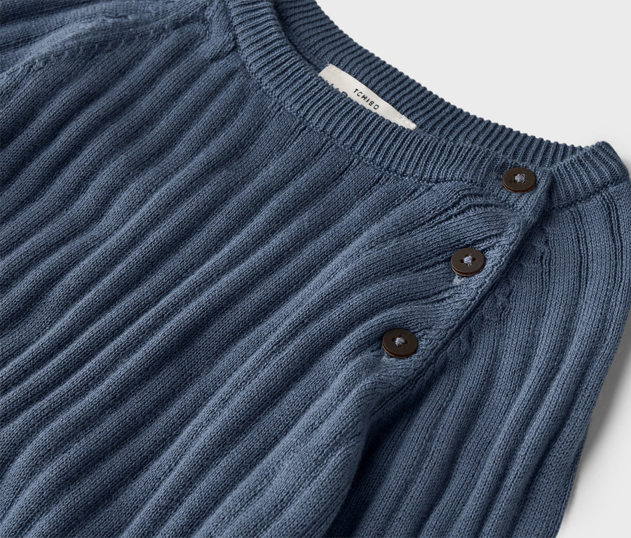 Gros plan d'un pull tricoté bleu foncé côtelé avec trois boutons au col.