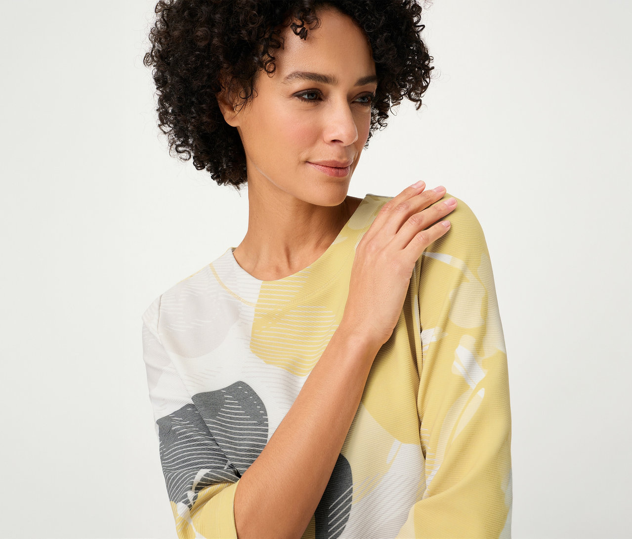 Une femme aux cheveux bouclés porte un sweat-shirt Olsen « Ottoman » à motifs jaunes, gris et blancs.