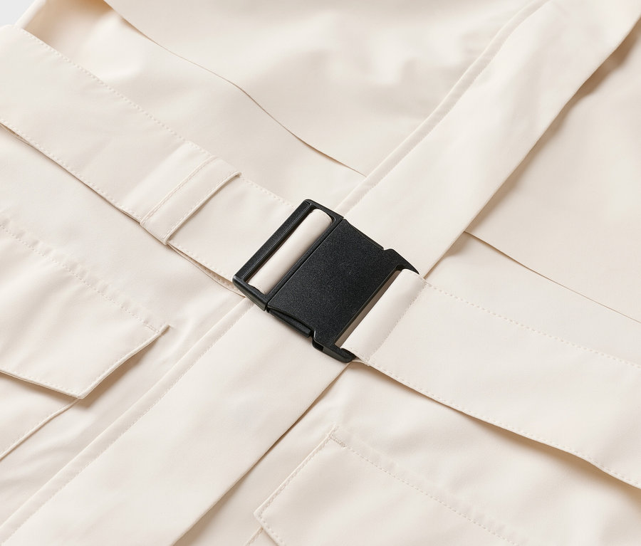 Gros plan d'un vêtement beige avec des poches et une fermeture à boucle noire.