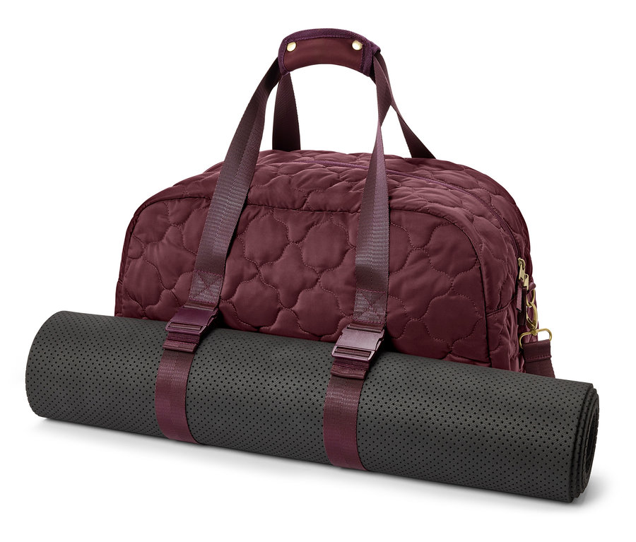 Un sac de sport bordeaux matelassé avec un tapis de yoga gris enroulé, fixé par des sangles bordeaux.