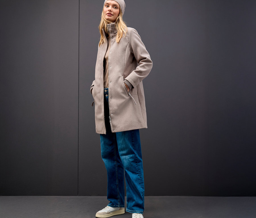 Femme portant un bonnet beige et un manteau court Street One sur fond gris.