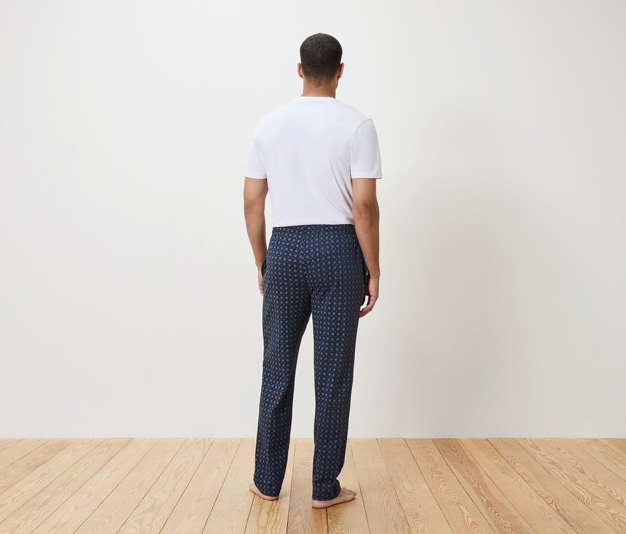 Homme vu de dos portant un t-shirt blanc et un pantalon de pyjama bleu marine à motif géométrique.