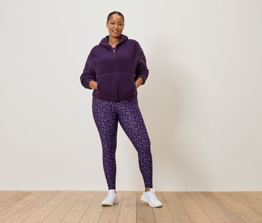 Femme portant un pull en polaire violet à demi-fermeture éclair et un legging violet à motif léopard, avec des baskets blanches.