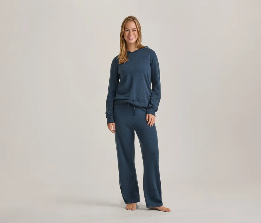Femme souriante debout, vêtue d'un sweat à capuche bleu à manches longues et d'un pantalon large assorti.