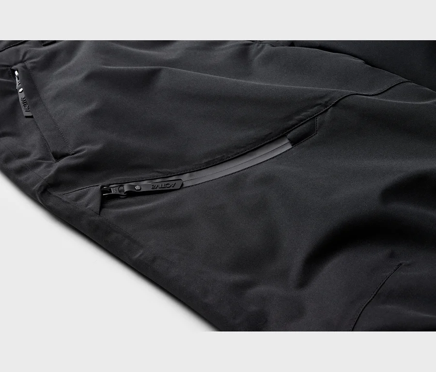 Gros plan sur un tissu technique noir avec deux poches zippées ; une horizontale et une diagonale, toutes deux avec des tirettes « ACTIVE ».