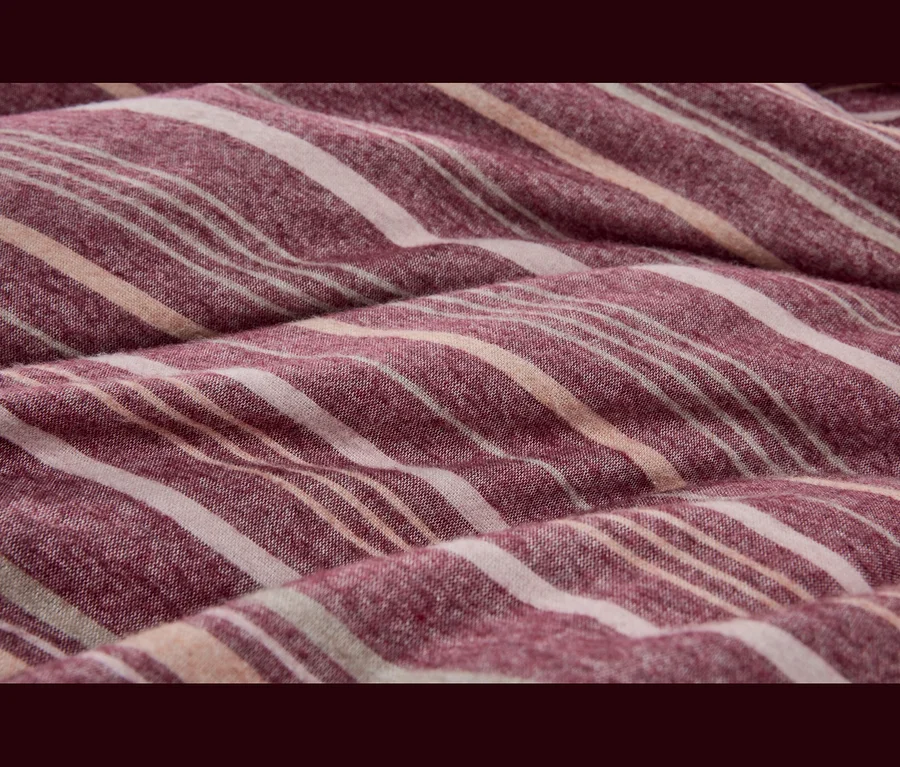 Gros plan d'un tissu doux et plié avec des rayures rouge-violet, blanc cassé et pêche clair.