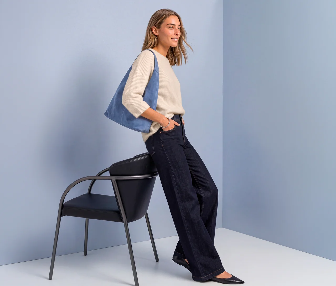 Femme portant un pull en maille Street One beige, un jean foncé et des ballerines noires, appuyée sur une chaise noire, avec un sac bleu.