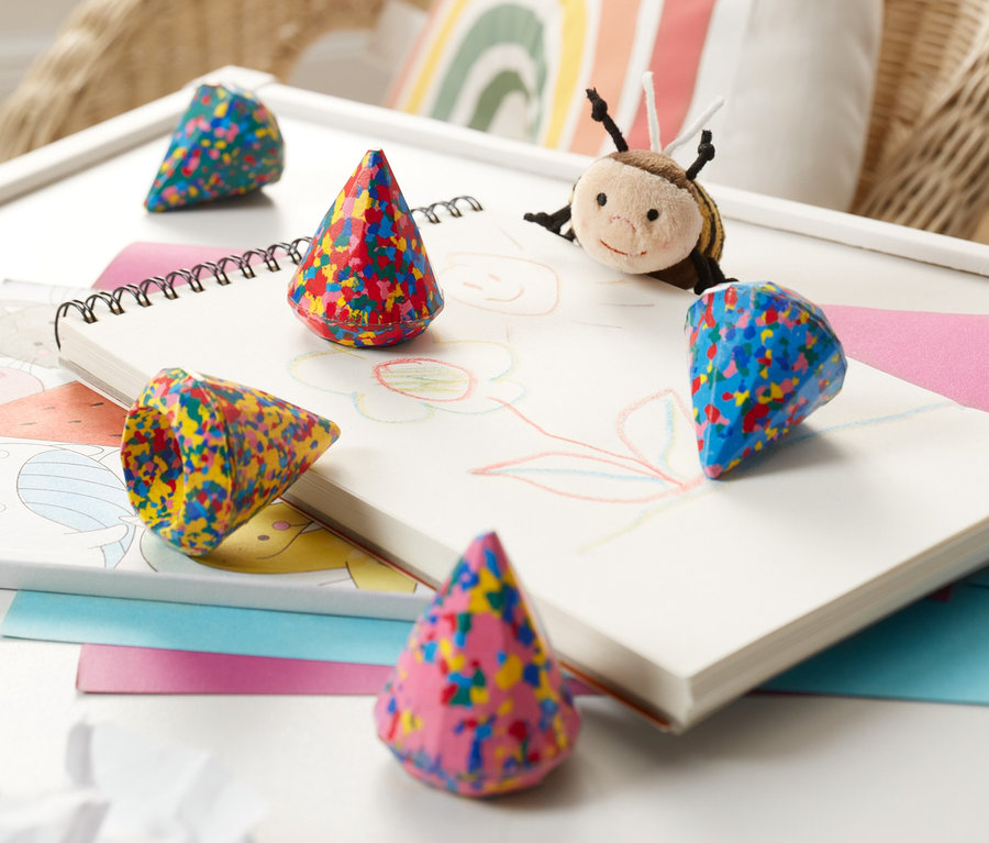 Sur une table, un carnet de croquis peint et des craies de cire confetti.