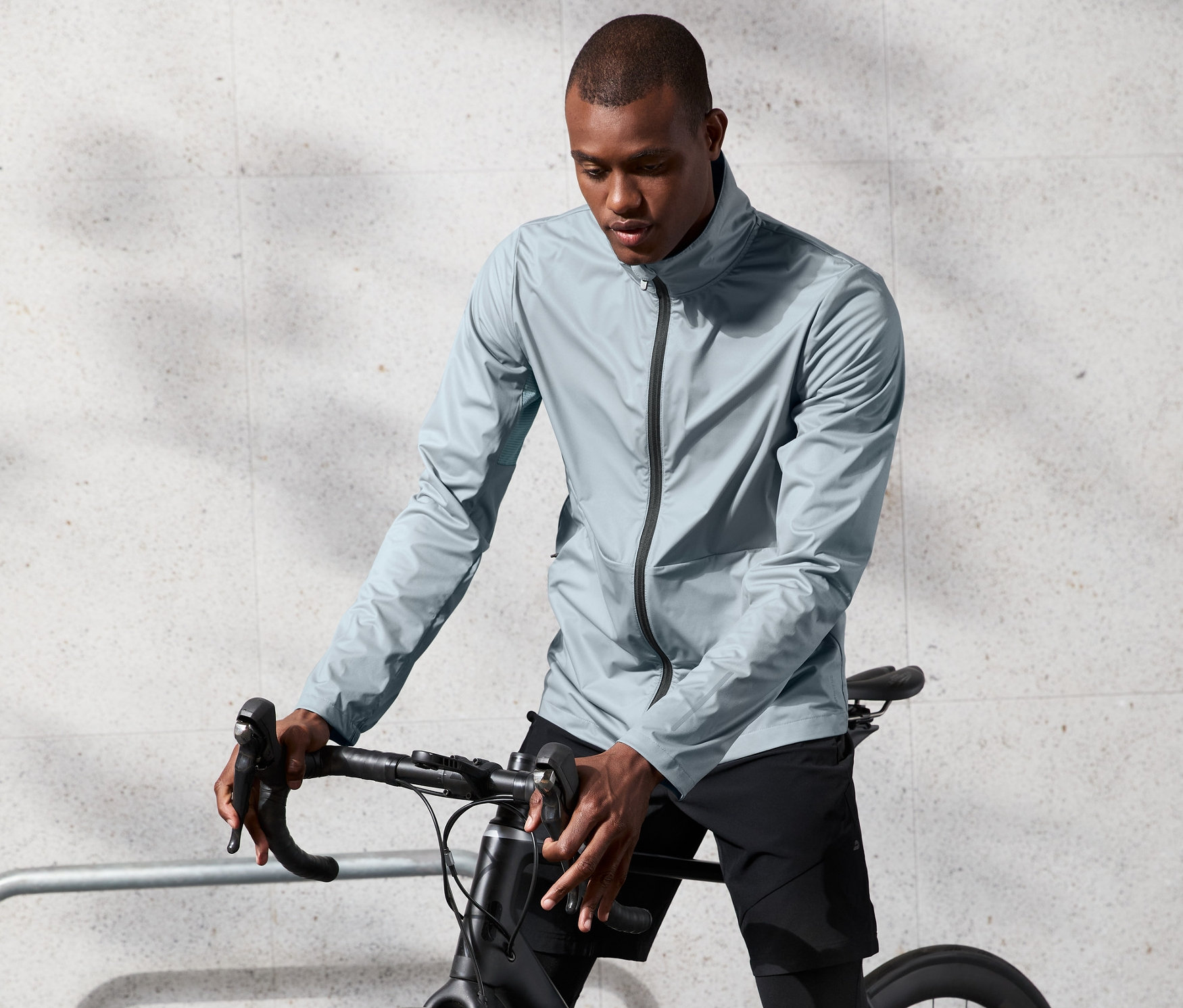 Un homme portant une veste fonctionnelle coupe-vent grise se tient à côté d'un vélo.
