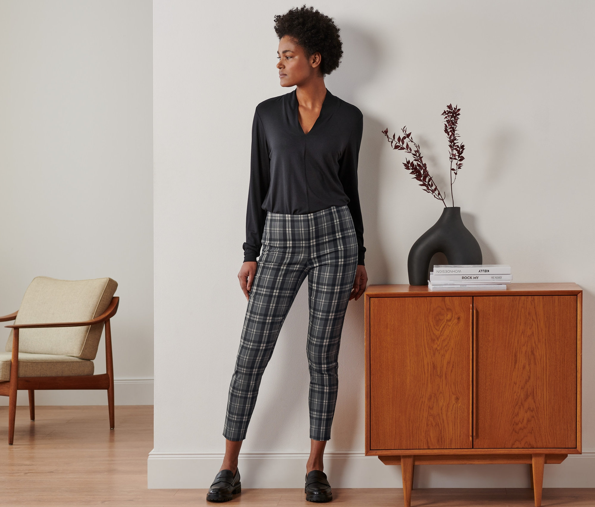 Femme posant en pantalon stretch à carreaux, haut noir et chaussures noires.