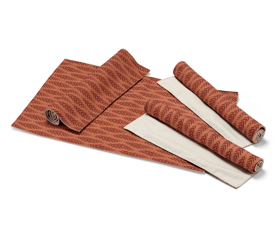 4 sets de table réversibles dépliés et enroulés avec motif de feuilles terracotta sur fond beige.