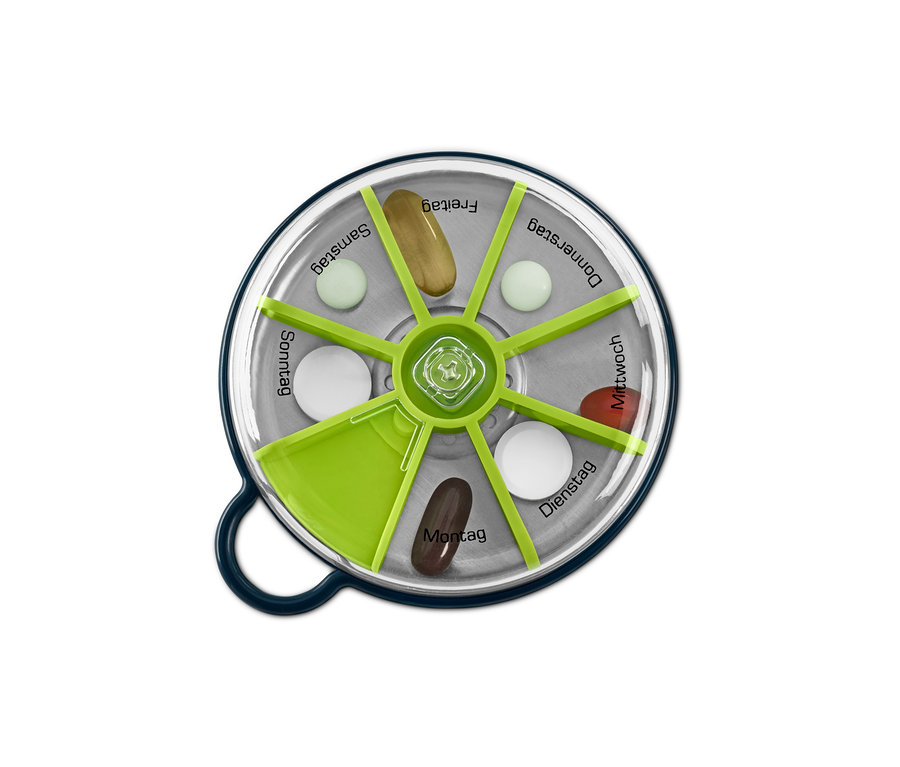Vue de dessus d'un pilulier rond transparent vert et argent avec différentes pilules dans des compartiments étiquetés avec les jours de la semaine.