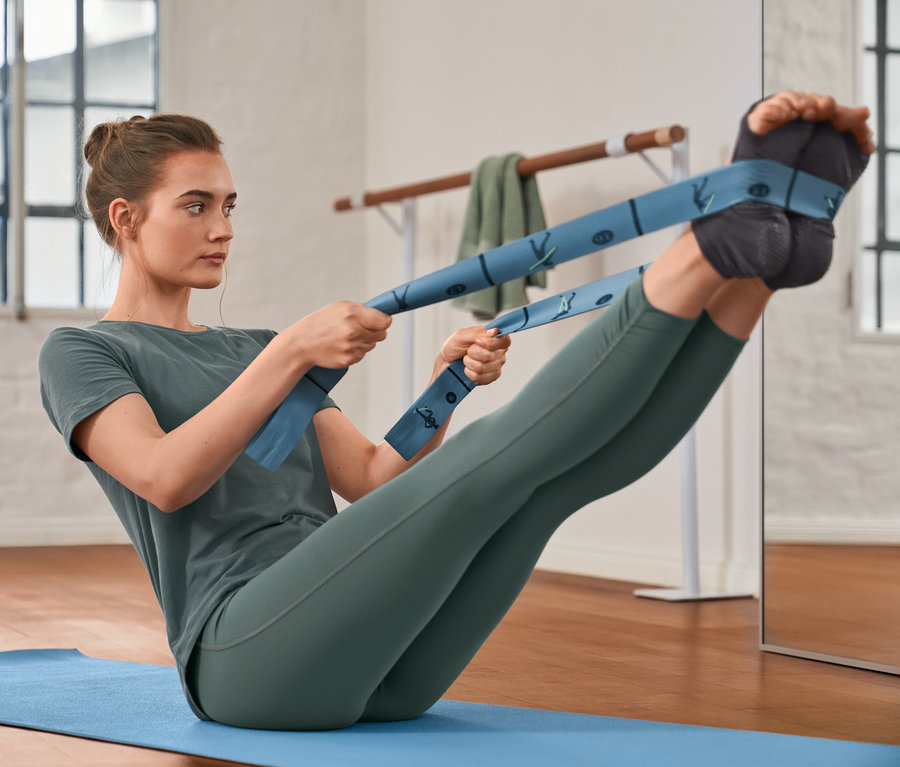Femme faisant des exercices avec une sangle élastique de fitness, portant un T-shirt de sport, un legging de sport modelant et des socquettes de yoga.