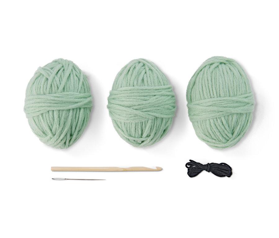 Kit DIY pour panier de Pâques décoratif en crochet : trois pelotes de laine vertes, un crochet, une aiguille et du fil noir.
