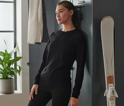 Femme appuyée sur un casier portant un t-shirt technique noir avec de la laine mérinos.