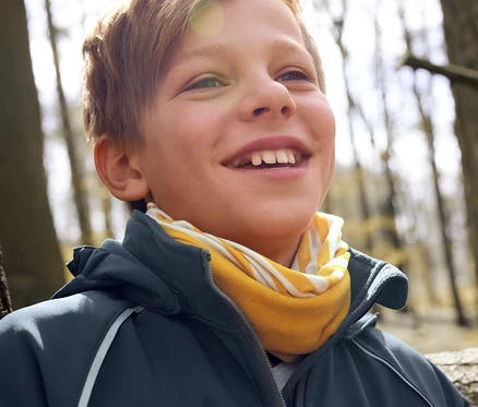 Un garçon souriant porte une veste softshell et un foulard multifonction.