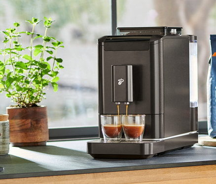 Sur un comptoir de cuisine, une machine à café entièrement automatique « Esperto2 Caffè » Granite Black prépare un expresso dans deux verres.