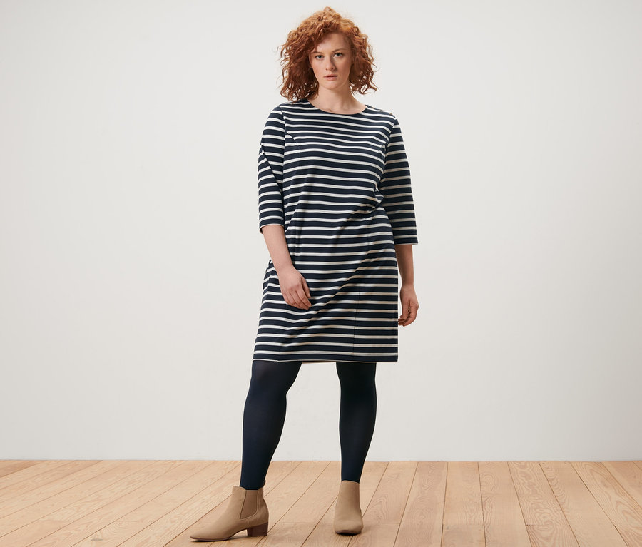 Une femme debout portant une robe molletonnée à rayures et 2 paires de collants fins.