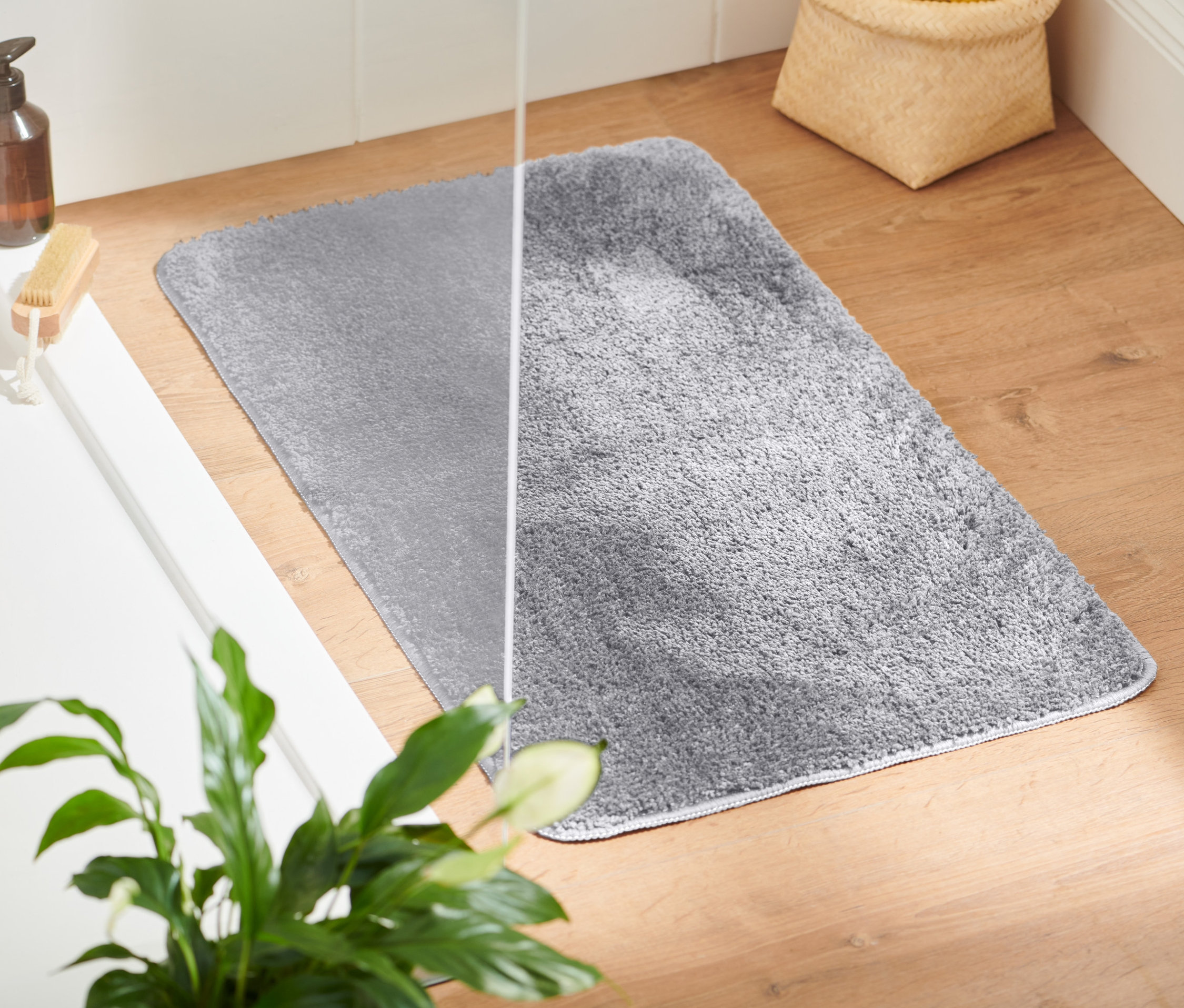 Un tapis de bain gris est posé sur un plancher en bois à côté d'une baignoire blanche.