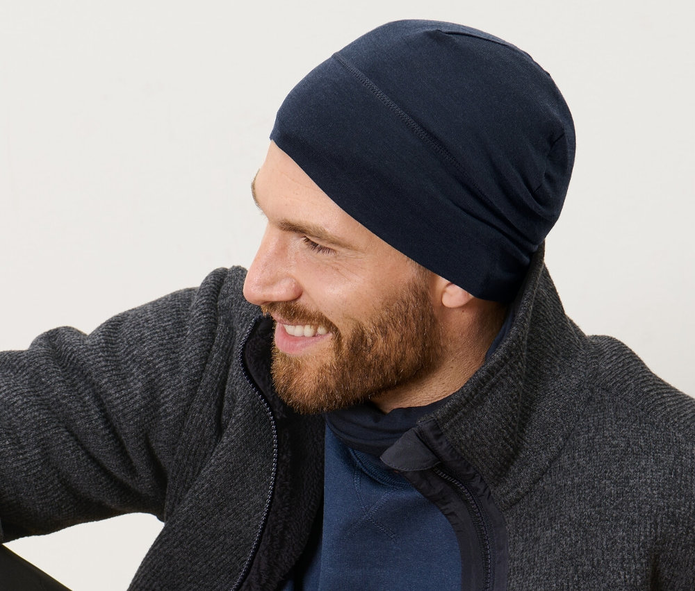 Un homme est assis sur un plancher en bois et porte un bonnet avec laine.