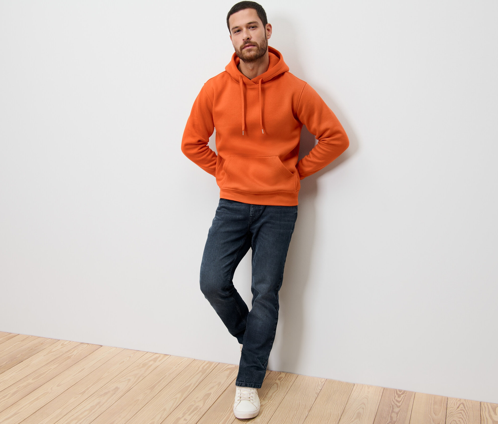 Un homme adossé au mur portant un sweat à capuche orange.