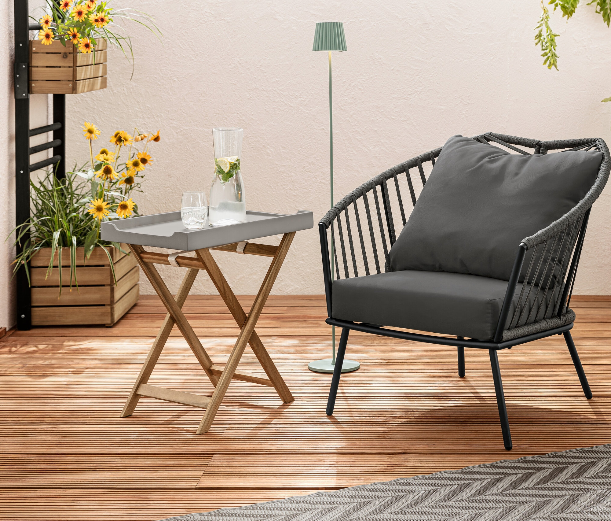 Sur une terrasse en bois se trouvent un fauteuil relax avec revêtement en tissu tressé, un tapis d’extérieur, env. 165 x 115 cm, taupe-gris clair, et un mur végétal « Elin » avec des fleurs. À l'arrière-plan, un lampadaire d’extérieur à LED rechargeable, sauge.