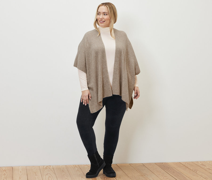 Une femme porte une cape en tricot, un legging en velours côtelé et un t-shirt col roulé à manches longues blanc crème.