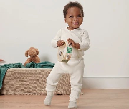 Un bambin noir souriant tient un tambourin et porte un pantalon en maille pour bébés.
