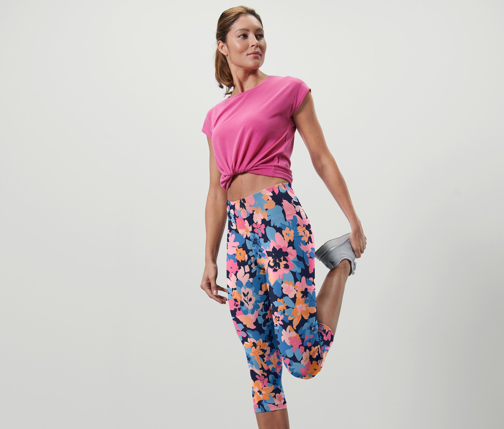 Femme étire la jambe en corsaire de sport à motifs floraux.