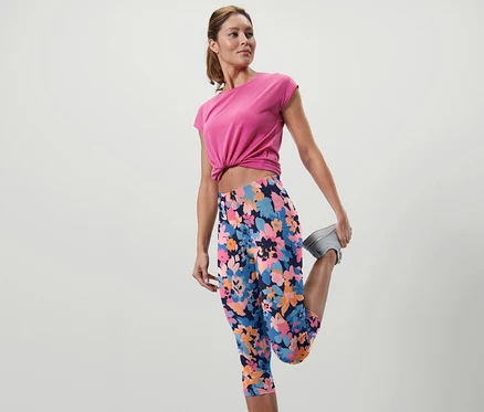 Femme étire la jambe en corsaire de sport à motifs floraux.