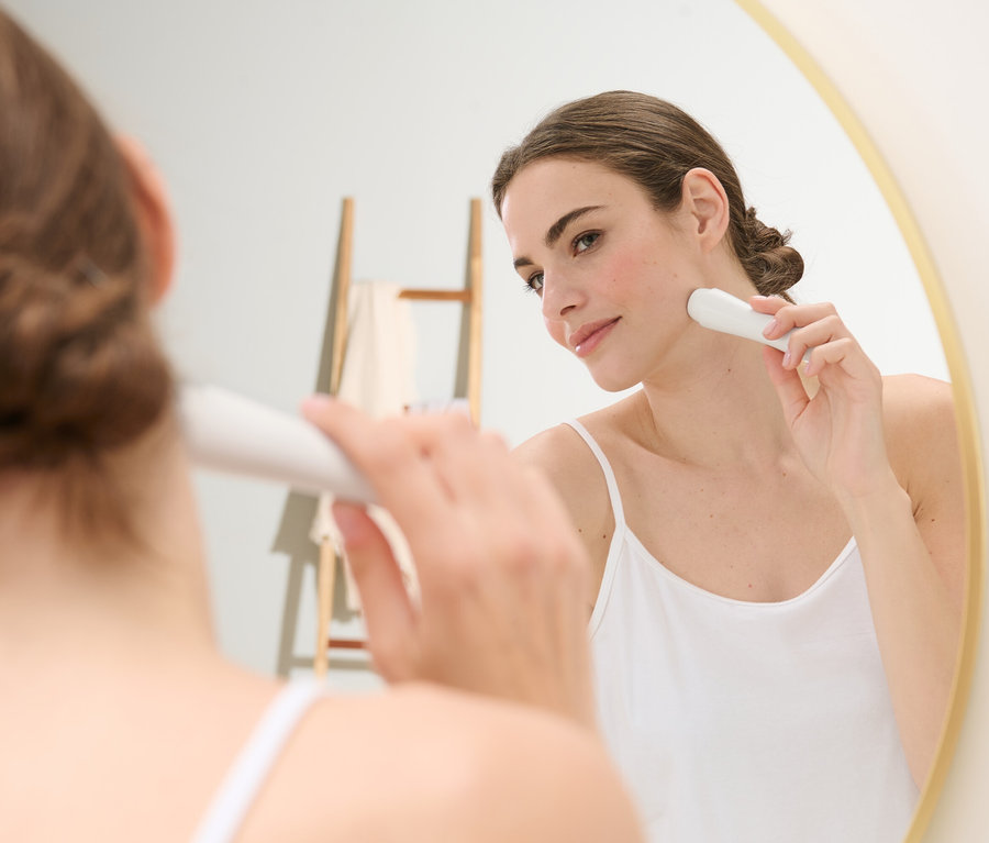 Une femme utilise un épilateur électrique pour le visage devant un miroir.