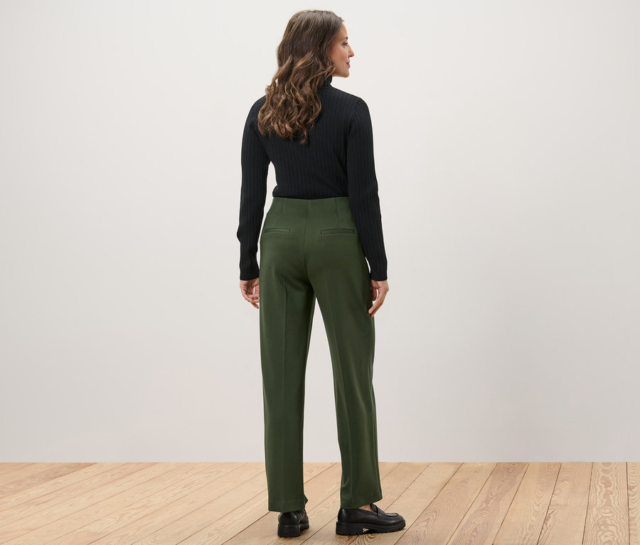 Une femme, vue de dos, porte un haut noir et un pantalon en jersey vert.