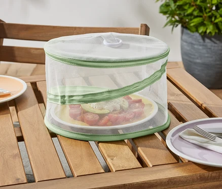 Une mini-cloche de protection pliable est posée sur une table en bois et protège une assiette de nourriture.