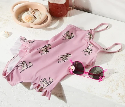 Un maillot de bain à ruché rose à motif zébré est posé à côté de lunettes de soleil roses, d'une boisson dans un verre et d'un sac de plage.