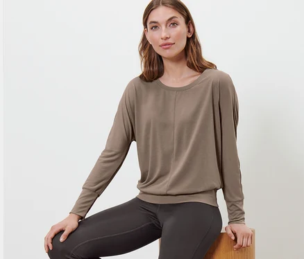 Femme assise sur des marches en bois et portant un t-shirt de sport et de yoga taupe.