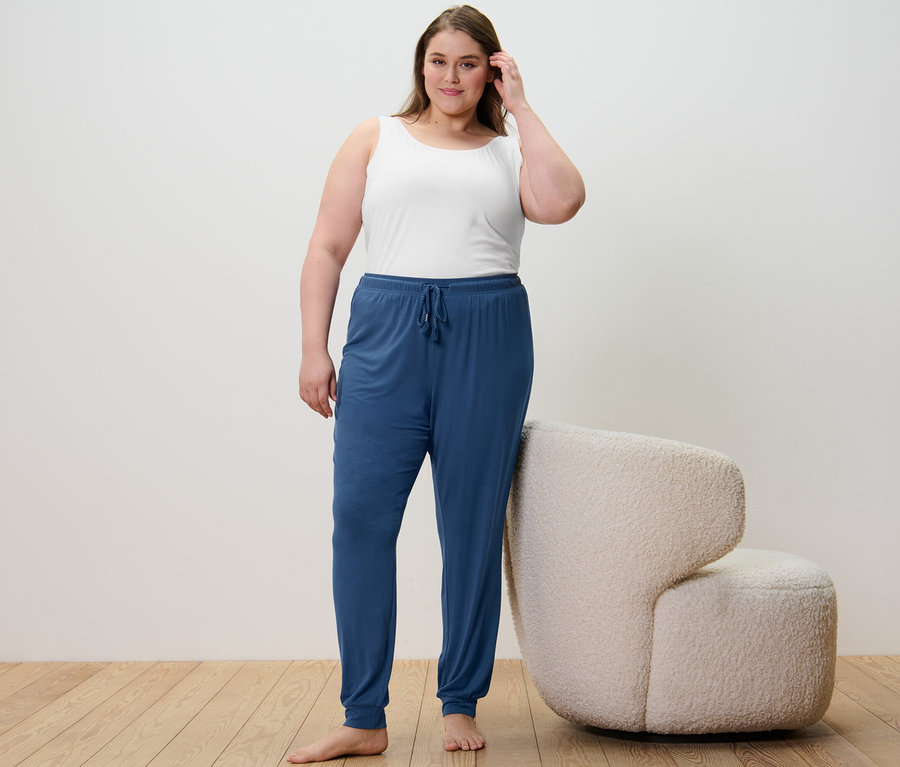 Une femme debout portant 2 débardeurs bleu foncé/blanc et un pantalon de pyjama.