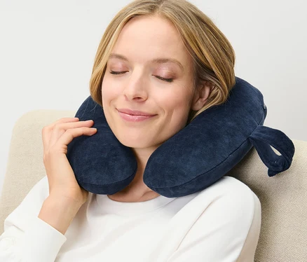 Femme assise dans un fauteuil avec un coussin de nuque bleu marine en mousse à mémoire de forme autour du cou.