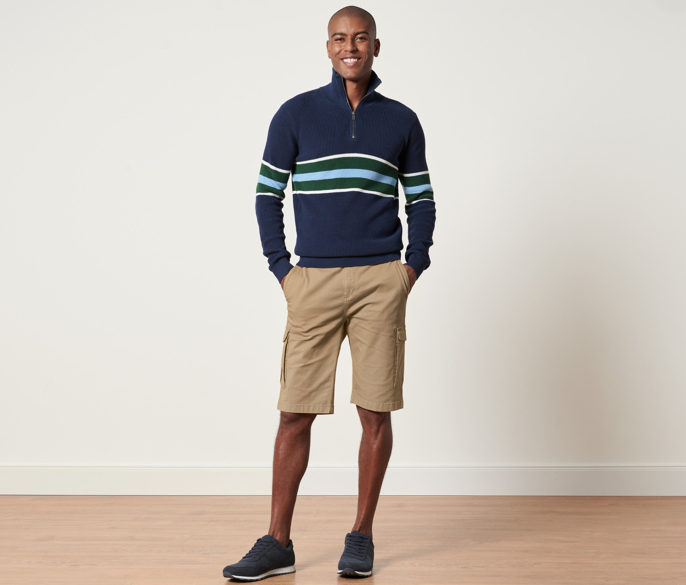 Un homme se tient debout et pose, portant un pull rayé marine et un short cargo sable.