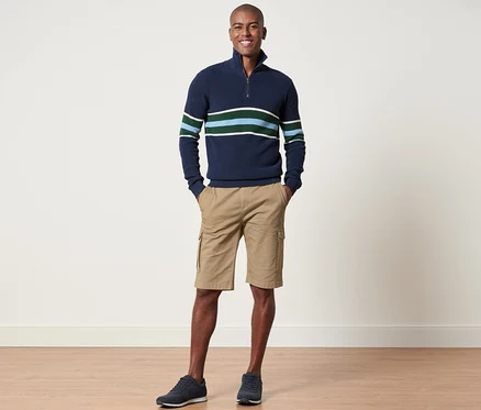 Un homme se tient debout et pose, portant un pull rayé marine et un short cargo sable.