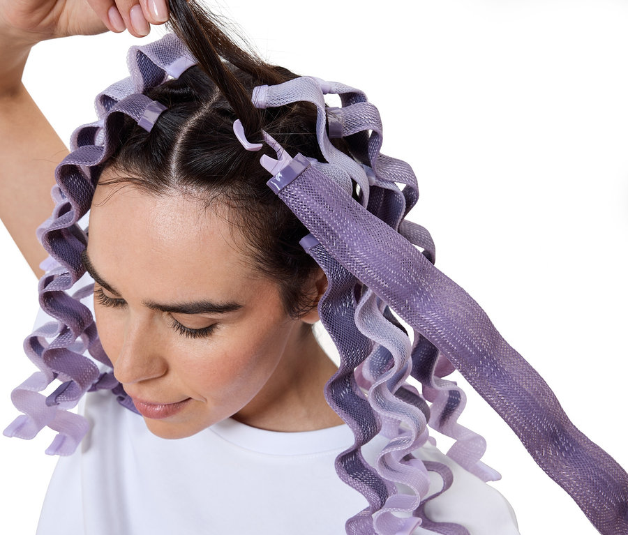 Femme enroulant ses cheveux avec des bigoudis violets.