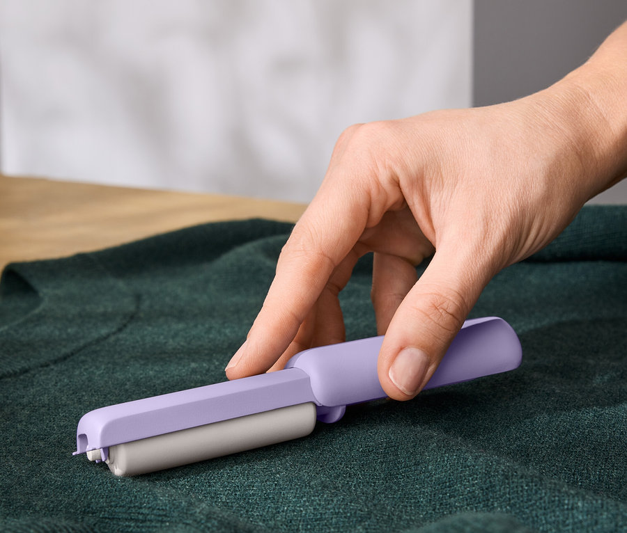 Une main utilise un rouleau anti-peluches violet sur un pull vert.
