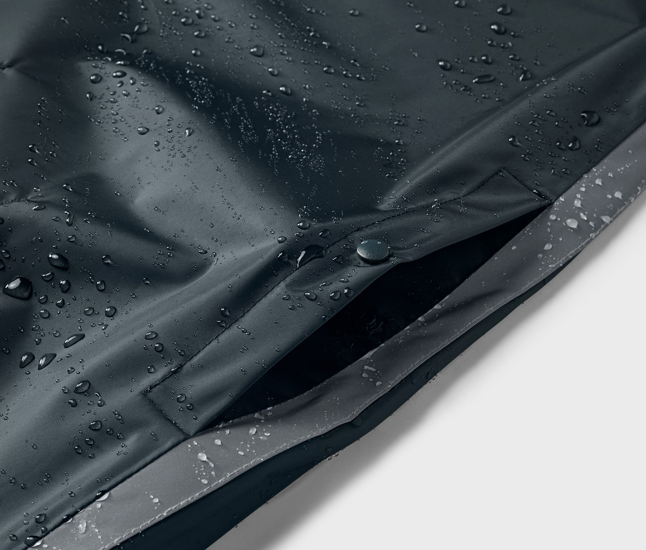 Gros plan sur un poncho de pluie bleu pour enfant avec des gouttes d'eau et une poche.